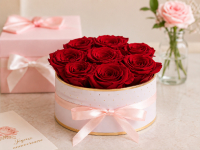Boîte ronde rose pâle garnie de roses éternelles rouges avec nœud en satin