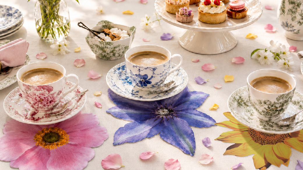 Sommerliche Kaffeetafel mit floralen Glasuntersetzern in Rosa, Blau und Gelb, Kaffeetassen und kleinen Törtchen