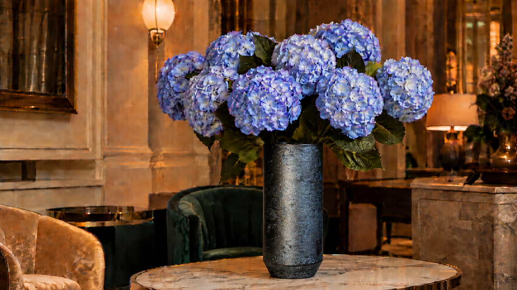 Blue and lilac artificial hydrangeas arranged in a dark decorative vase