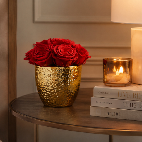 Kleines rotes Infinity Rosen Gesteck in goldfarbener Keramikvase auf einem eleganten Beistelltisch