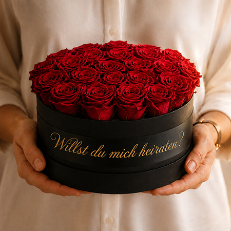 Person hält schwarze Rosenbox mit roten konservierten Rosen und goldener Aufschrift Willst du mich heiraten