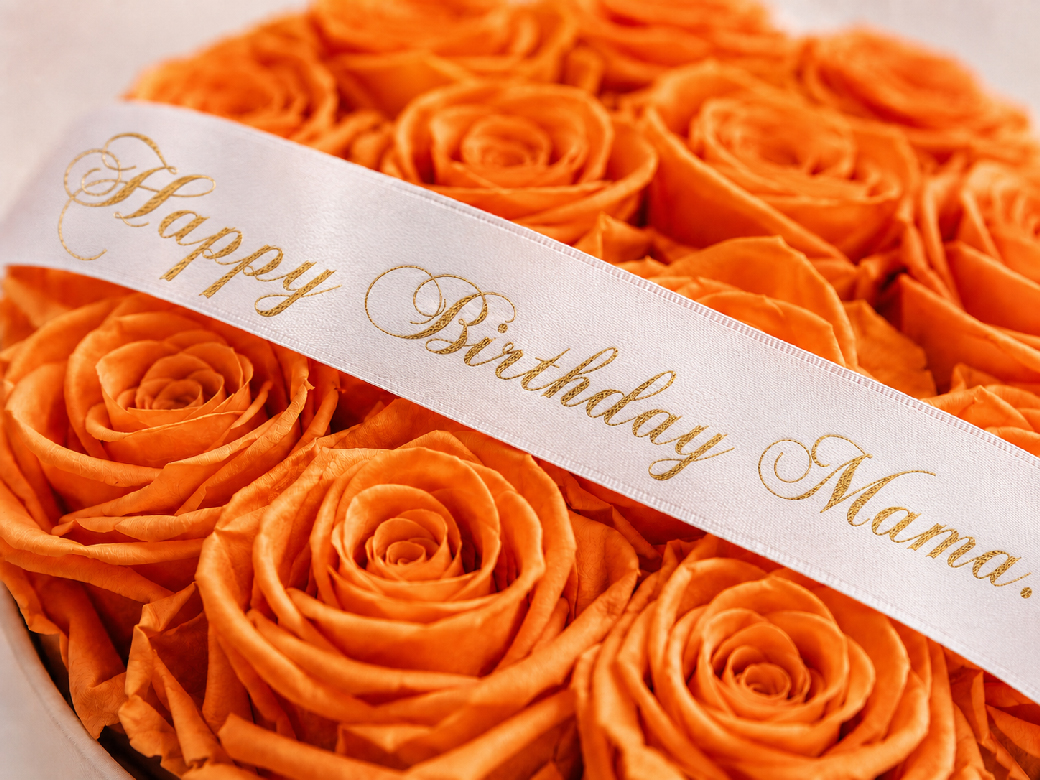 Personalisiertes Satinband mit goldener Geburtstagsbotschaft auf orangefarbenen Infinity Rosen